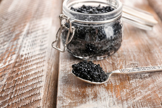 Spoon and glass jar with black caviar on wooden table