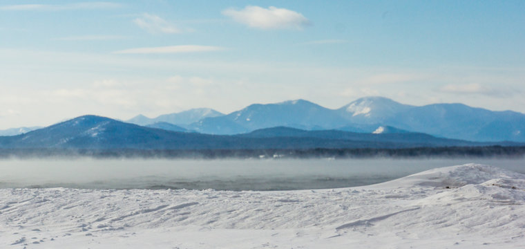 Frigid Winter Morning With Misty Steam Rising Off The Lake With The Adirondack Mountains Across The Lake In New York 
