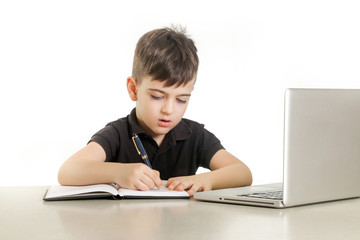 Young boy making notes in front of laptop 