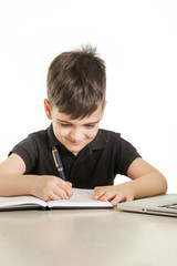 Young boy making notes in front of laptop 