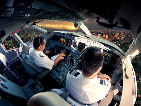 Cockpit of modern passenger jet aircraft. Pilots at work. Aerial view of modern city business district and sunset sky.