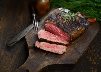 grilled steak with rosemary on a cutting board on a black background