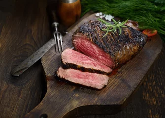 Wall murals Steakhouse grilled steak with rosemary on a cutting board on a black background