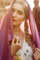 Close-up portrait of a beautiful young woman with a gorgeous bindi on her forehead. Long blonde hair is tangled in hairstyle. She is covered with a beautiful purple silk scarf with small prints.