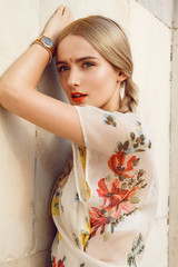 Close-up portrait of a beautiful young woman with gorgeous bindi on her forehead. Long blonde hair is tangled in wonderful hairstyle. And she is dressed in a pretty dress with floral print.