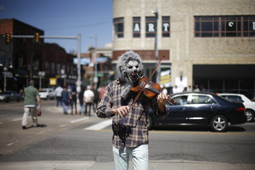 Man in a wolf mask playing violin downtown in front a city scene with word art above head.