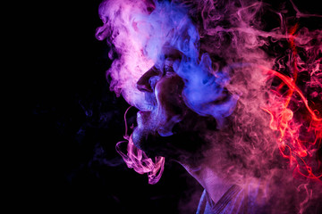 Man  is admiting puffs of steam from the electronic cigarette, cloud of colored smoke of red and...