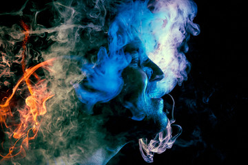 Man  is admiting puffs of steam from the electronic cigarette, cloud of colored smoke of blue,...