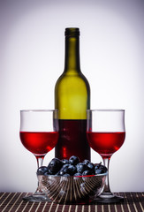 Bottle of red wine and wine glasses / open bottle of red wine, two glasses and a cup with grapes stand on a table