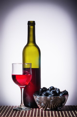 Bottle of red wine and a glass / open bottle of red wine, glass and bowl with grapes stand on a...