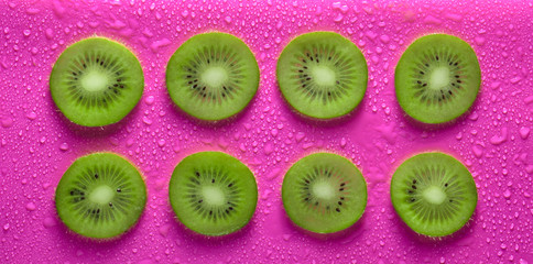 Slices of kiwi in water drops on a pink background. Fruit concept.