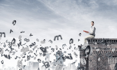 Man on roof edge reading book and symbols flying around