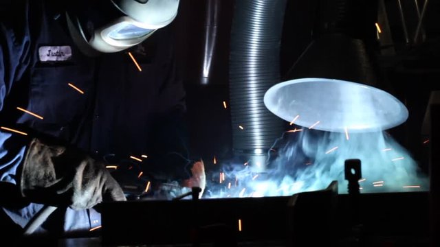 Medium shot of welder with mask, welding and vent sucking up fumes with sparks.
