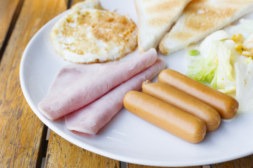 Breakfast - sausage, ham, fried egg, bread on white plate