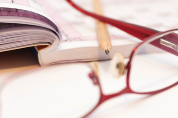 Sharp pencil in focus, eyeglass and crossword close up macro shot.