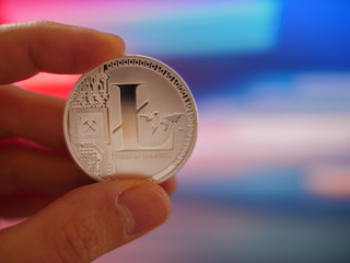 Hand holding silver litecoin LTC coin on colorful background, closeup.