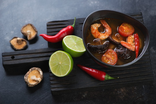 Bowl of Tom Yum soup on a black wooden serving board with some of its cooking components, studio shot