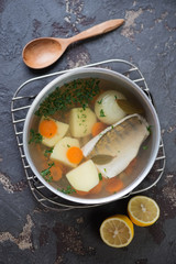 Kettle with sudak fish soup on a metal cooling rack, brown stone background, top view, vertical shot