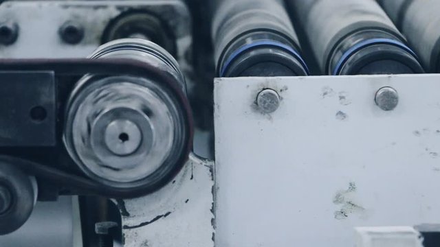  Industrial conveyor line, rotating rollers, moving feed belt and adjacent relevant equipment. Selective focus. Industrial background.	Closeup.