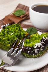 Fresh muffins with spinach, desiccated coconut, chocolate glaze and cup of coffee