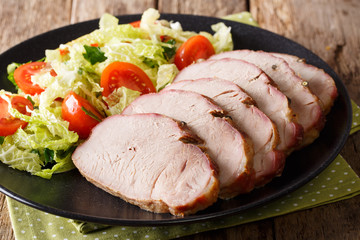 Delicious baked pork fillet with fresh vegetable salad close-up on a table. horizontal