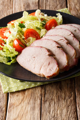 Sliced roasted pork fillet with fresh vegetable salad close-up on a table. vertical