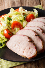 Sliced roast pork tenderloin with vegetable salad close-up on a plate. vertical