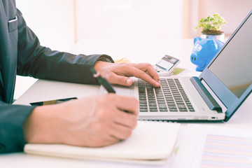 Close up shot businessman writing notes on notebook at office. Businessmen are using a laptop computer on a desk. Close up of hand of businessman typing on keyboard.