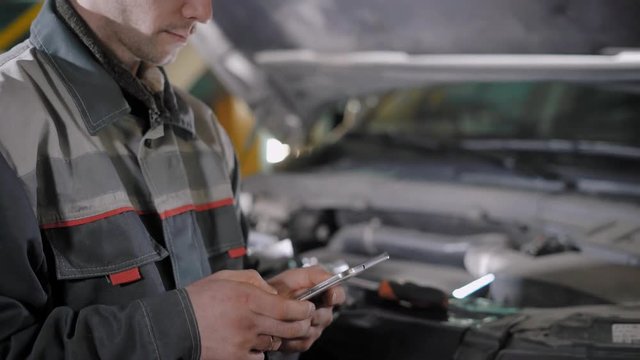 auto mechanic is using tablet for calculating value for a car repair and filling up a profile for automatic diagnosis