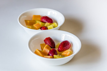 Colorful fresh fruit salad in white bowls, side view..Two white dishes of cut up healthy mixed fruit, white background, closeup.