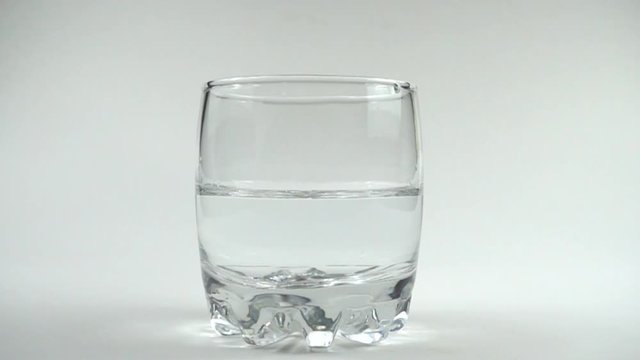 Cubes of ice fall in a glass with water. Slow motion. 