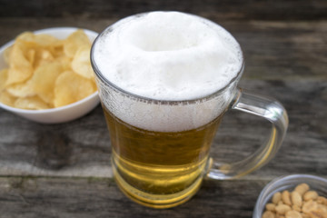 Mug with foam beer, chips and nuts on a wooden background.