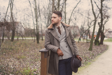 Handsome elegant man in the park wear suit and coat.