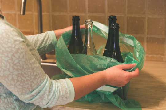 Woman hold garbage bag with empty glass bottles in the kitchen, recycling.