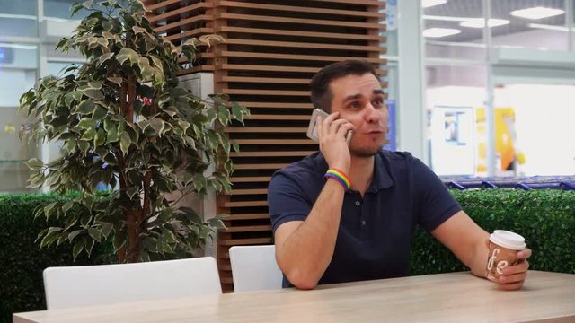 young man with rainbow symbolism in a cafe, talking on the phone and smiling