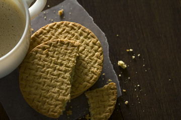 Top view of hot coffee drink in white coffee cup and partialy eaten or chipped biscuits or cookies on baking parchment paper