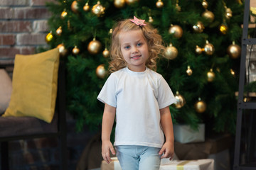 Cute little girl in a white T-shirt is standing near the Christmas tree. Mock-up.