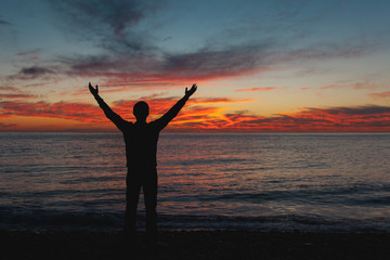Man with arms up wide open silhouette on sea sunset. Travelling alone. Meditative nature and human concept.