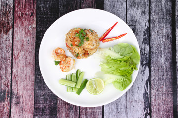 Fried rice with shrimp topped sliced red hot chili pepper,sliced cucumber ,halved green lemon and garlic on white plate.