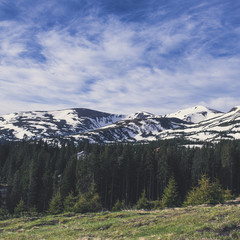 Obraz premium Spring mountain landscape with snow and fir forest. Dramatic clouds lying on the horizon and sun is shining. Natural outdoor travel background in retro hipster style.