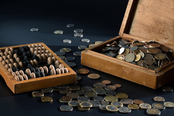 A pile of coins in a box and wooden abacus