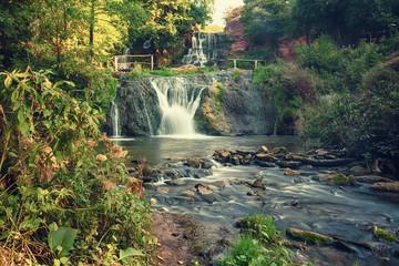 Beautiful mountain rainforest waterfall with fast flowing water and rocks, long exposure. Natural seasonal travel outdoor background in hipster vintage style