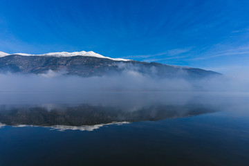 The snow covered mountain totally reflects in the lake of Ioannina in Greece