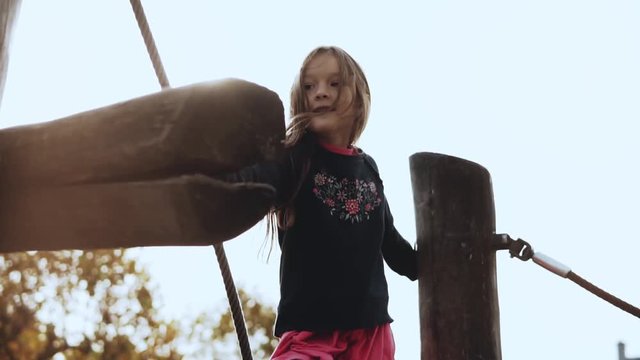 Portrait of little adorable girl on showground. Pretty smiling 7 year old girl goes over rope obstacles. Slow motion.