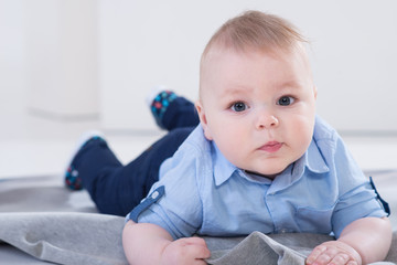 Cute little baby boy in blue shirt and jeans lying on the blanked and posing in the photo studio on white background