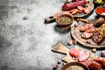 Different kinds of salami with spices and herbs on old boards.