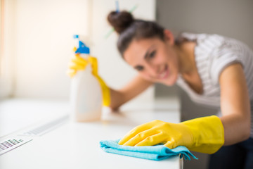 Close-up the young smiling woman in yellow gloves washing windowsill with rag and window cleaner...