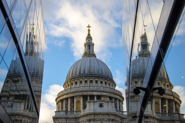 The dome of St Paul's Cathedral in London reflected in windows with blue sky and clouds