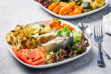 One pan dish, steamed fish steak, roasted vegetables, fresh tomato salad. Top view, copy space. 