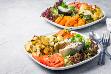Healthy dinner steamed fish roasted vegetables fresh tomato green salad.  Selective focus, copy space.